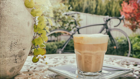 Glass of latte on a table with bicycle in the background